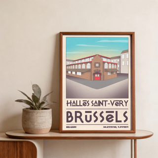Framed Brussels Architecture Art Print showing Halles Saint-Véry building in brown and red tones with blue sky on table next to plant
