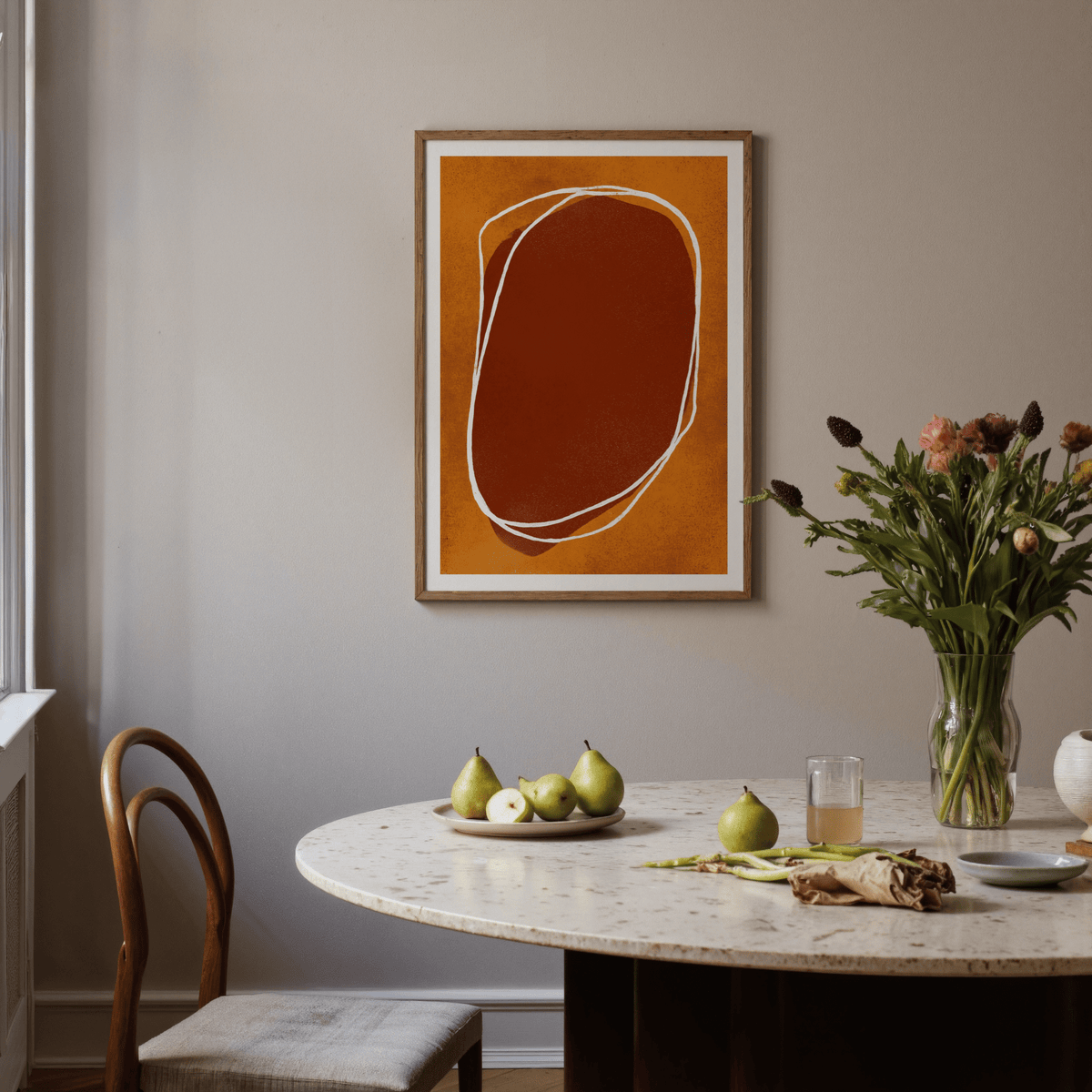 Abstract Earth Tone wall art with orange and brown shapes above a round dining table with pears
