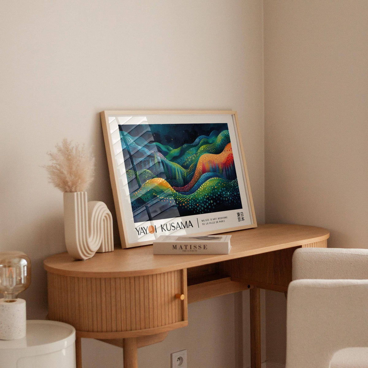 Horizontal Abstract Art leaning on a wooden desk with a cream vase and a book in a beige room