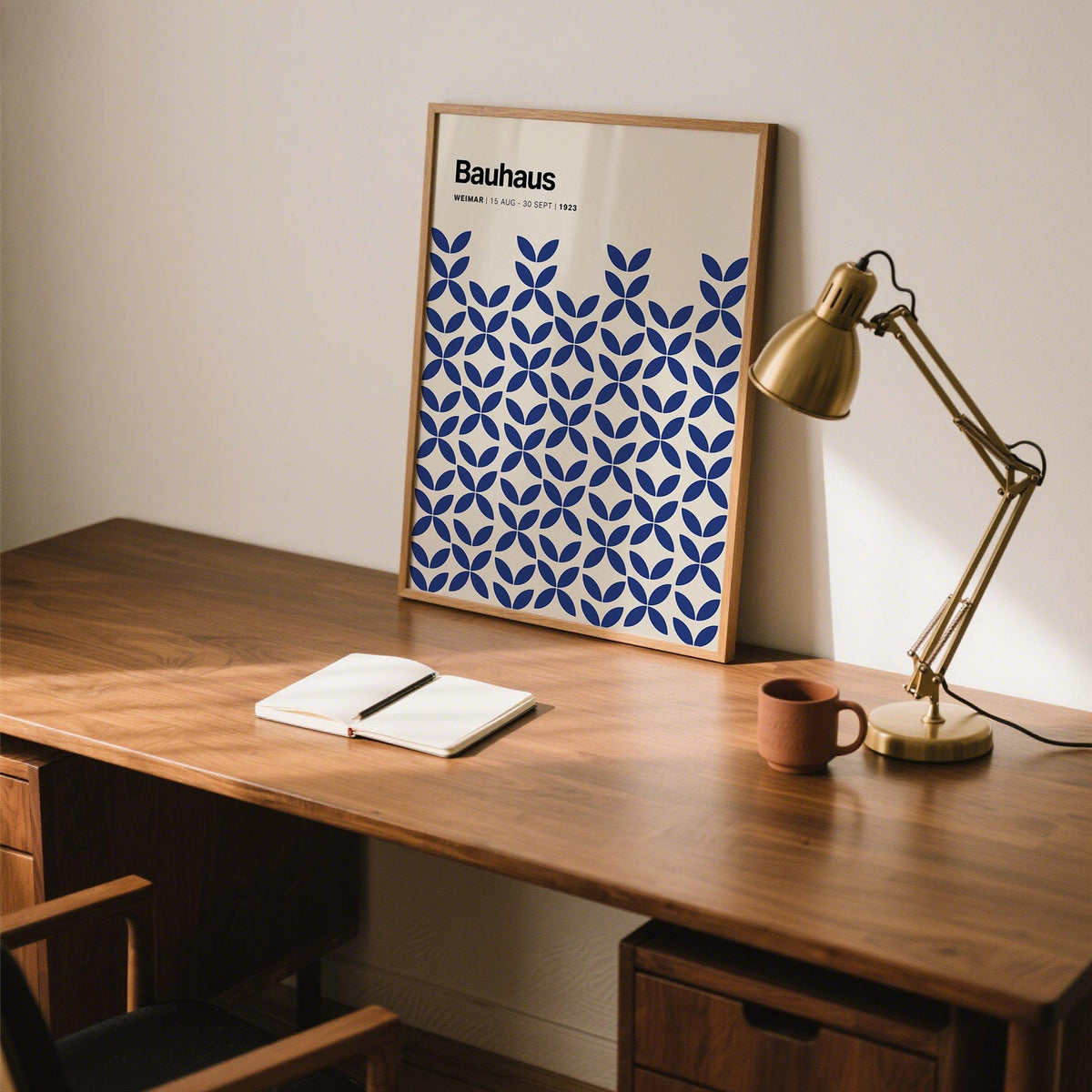 Simple wall art with blue geometric pattern leaning on a wooden desk next to a brass desk lamp