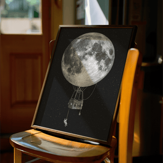 Framed Moon Hot Air Balloon Art with a wooden frame leaning on a chair in warm light