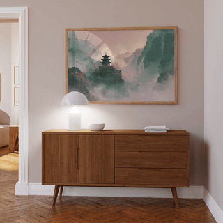 Misty Mountain Temple Art print with green and pink misty watercolour tones above a wooden sideboard and lamp