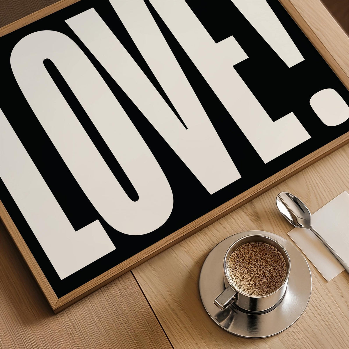 Framed LOVE typography close-up with black and white colours and a coffee cup on a wooden surface