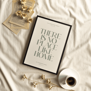 Framed No Place Like Home print with green typographic quote laid on fabric near coffee cup and dried flowers