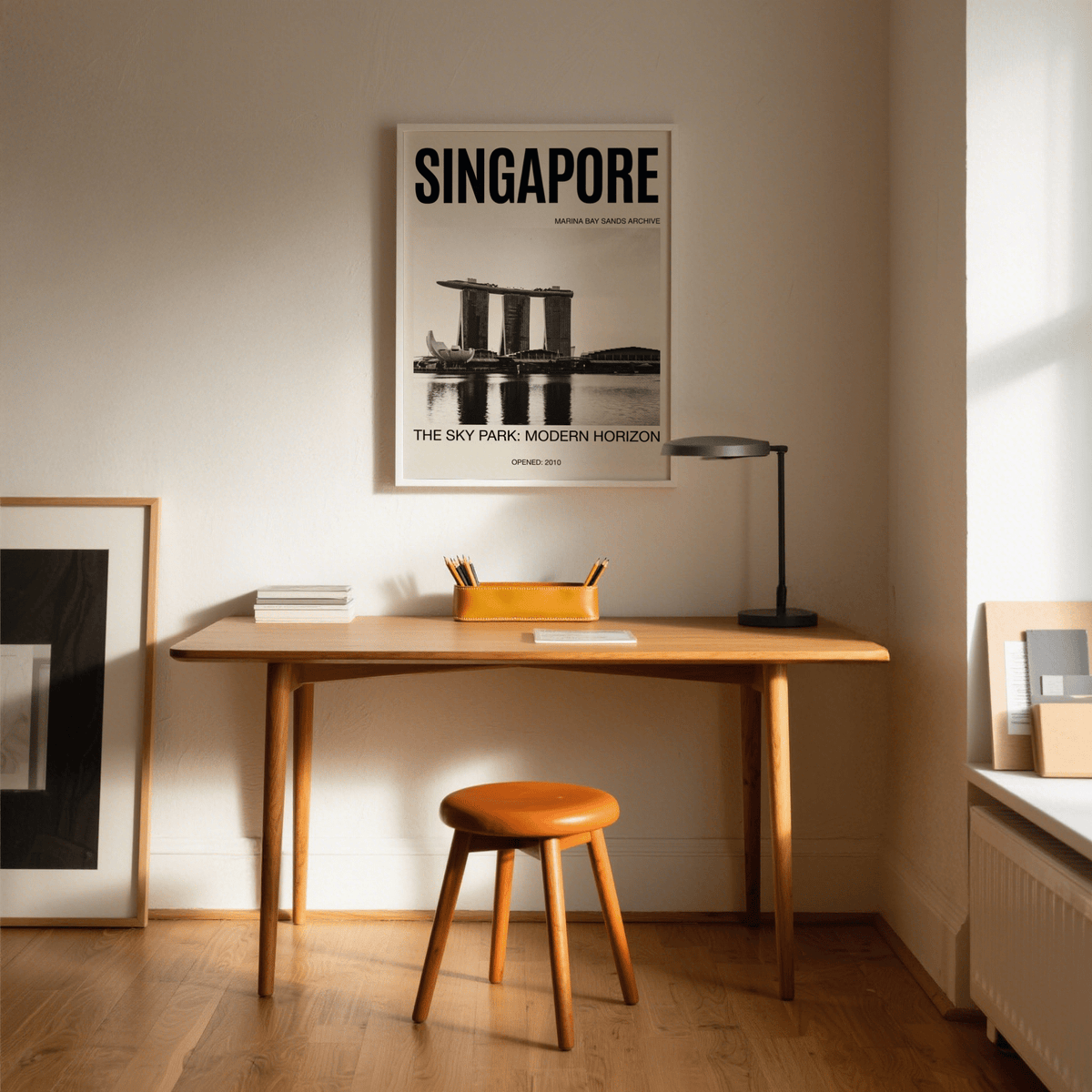Singapore Modern Architecture Art Print above a wooden desk and orange stool in a sunlit room