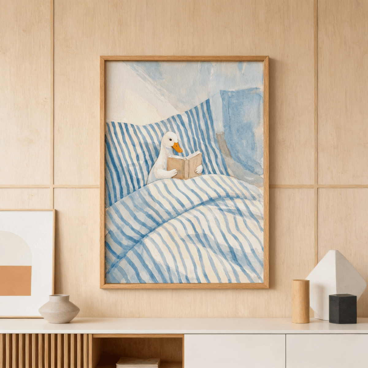Duck reading art print of a duck reading a book in blue striped bedding above a wooden sideboard