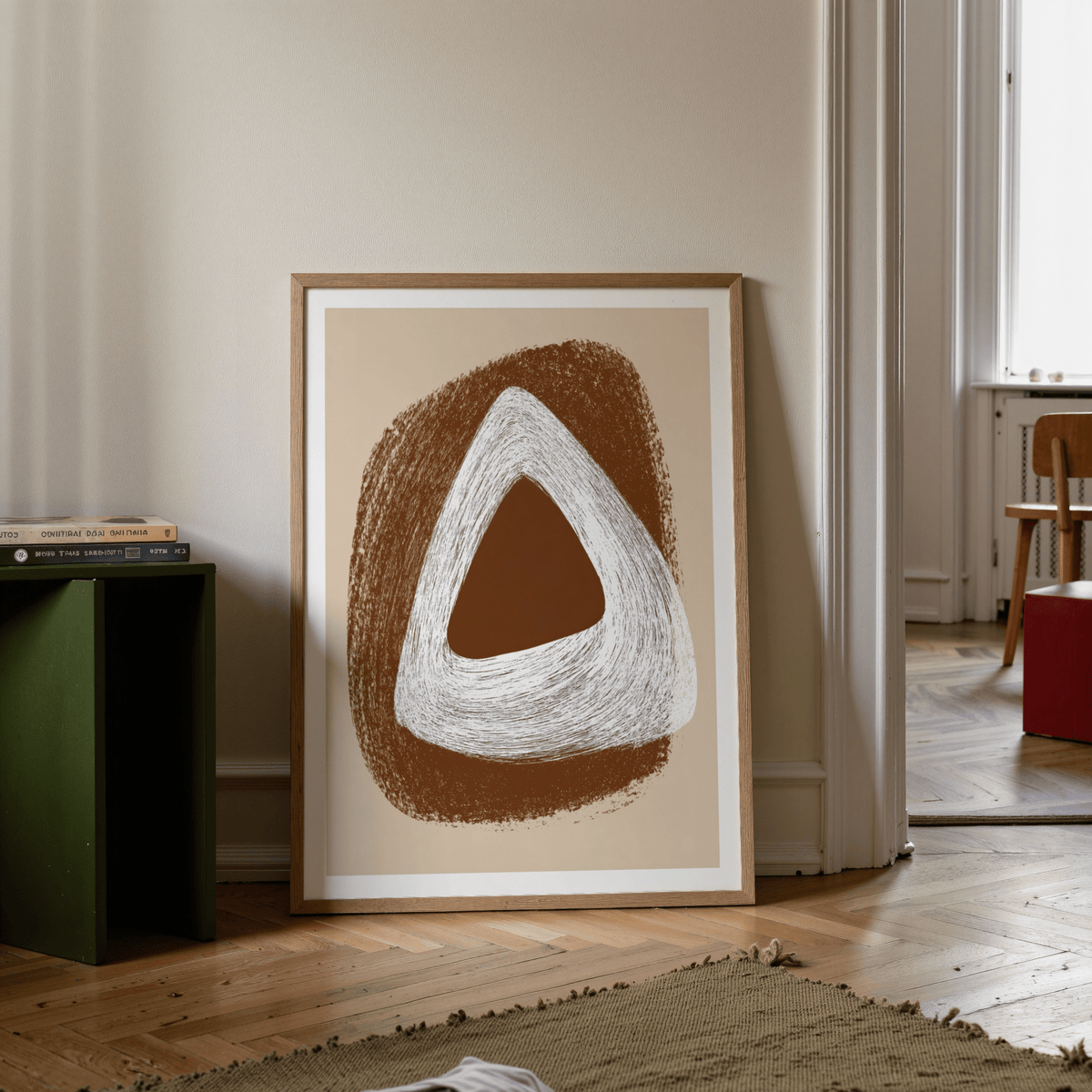 Print leaning on floor with abstract brown and white triangle shapes beside a green side table
