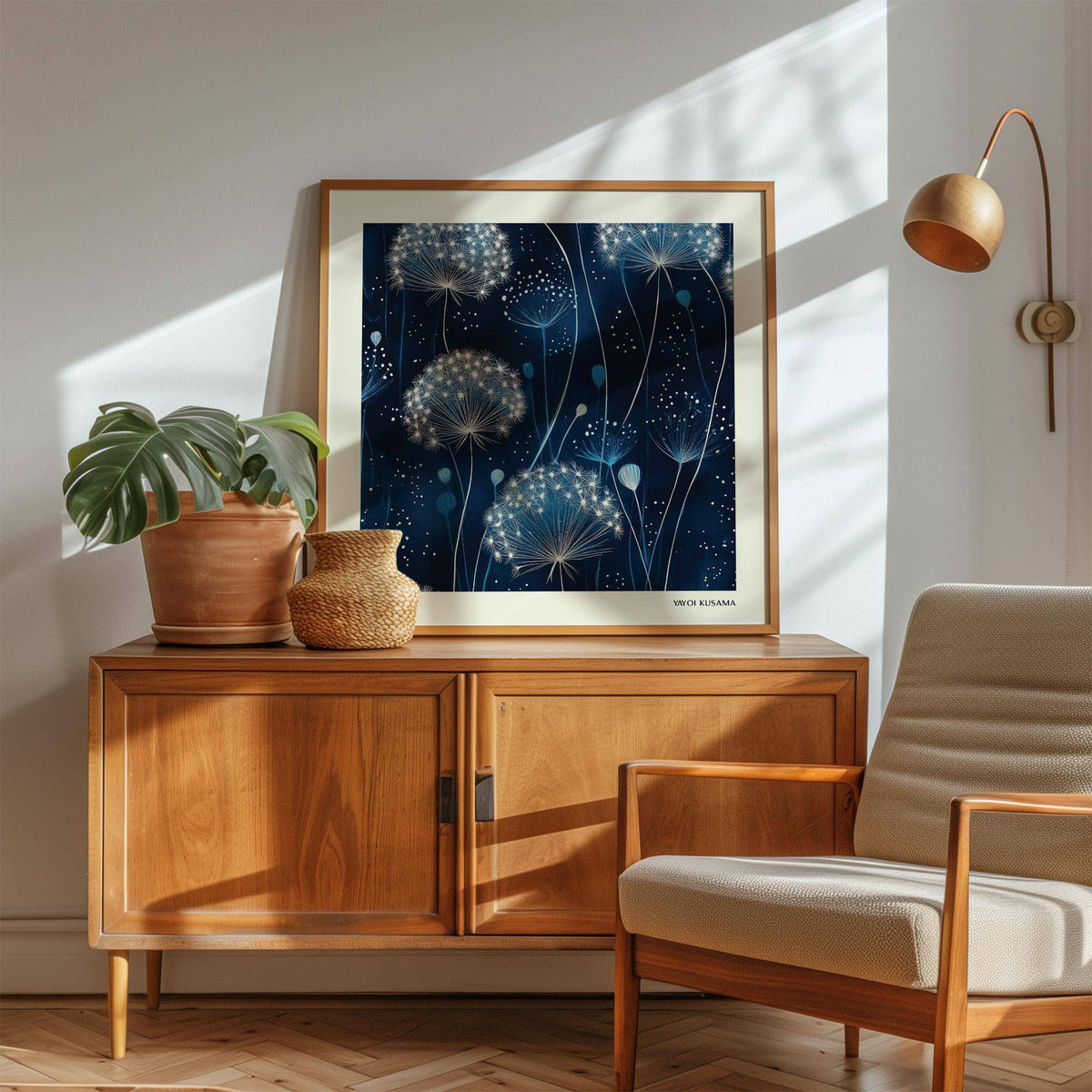 Blue art work of dandelion seed heads in white and blue tones on a wooden sideboard with a plant