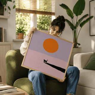 Minimalist Cat Art Print held by a woman showing a black cat silhouette and an orange sun