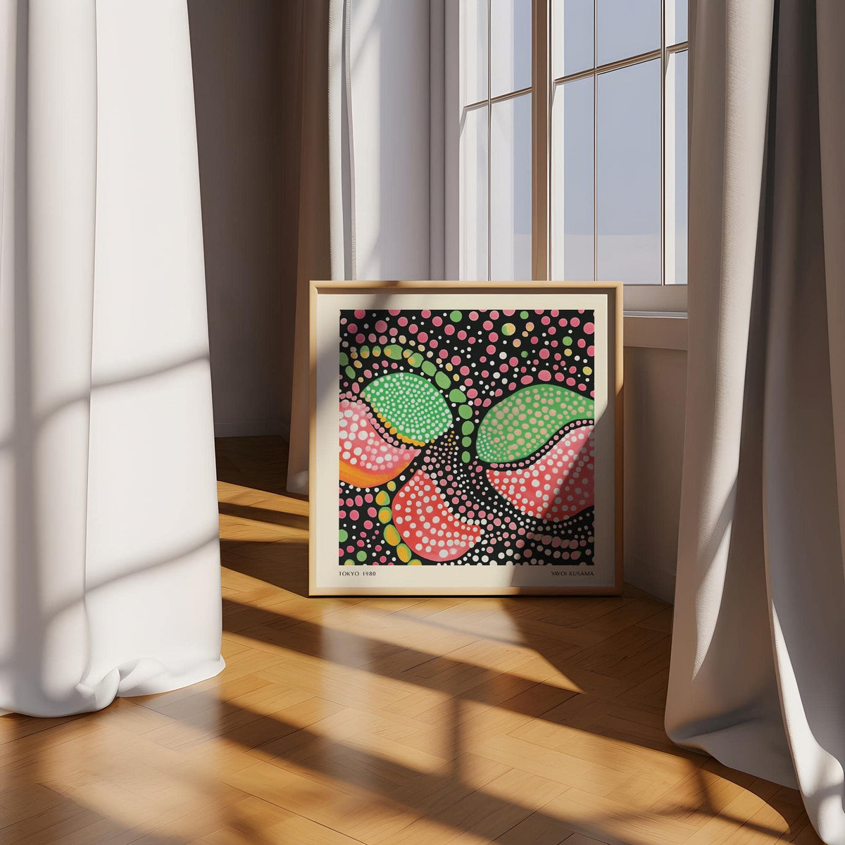 Print leaning on floor with green pink art of abstract fruit shapes against a window and light curtains