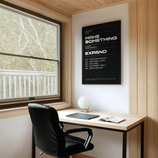 Wall Art Phrases framed print with white text on black above a wooden desk and black chair