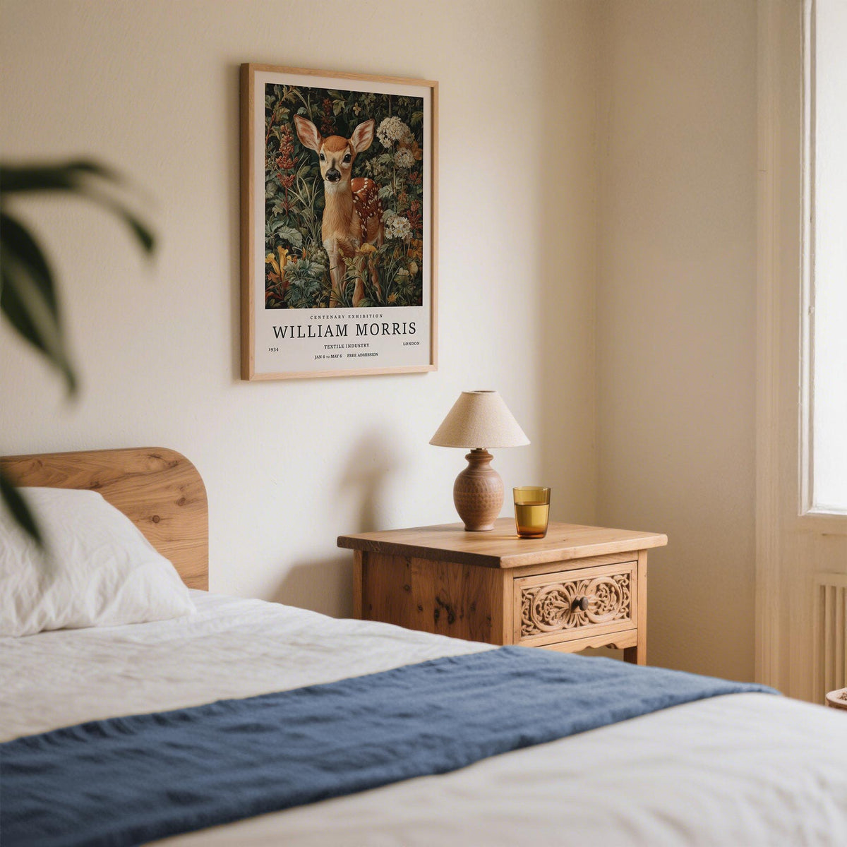 Forest art print of a fawn in detailed botanical foliage above a wooden bedside table in a bedroom