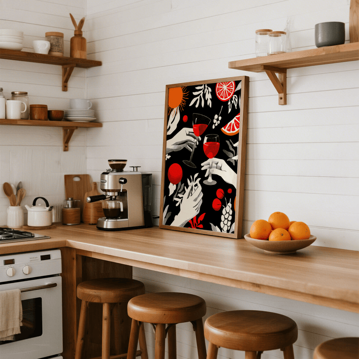 Celebration wall art of hands toasting with wine glasses in red black and white leaning on a kitchen counter beside a bowl of oranges