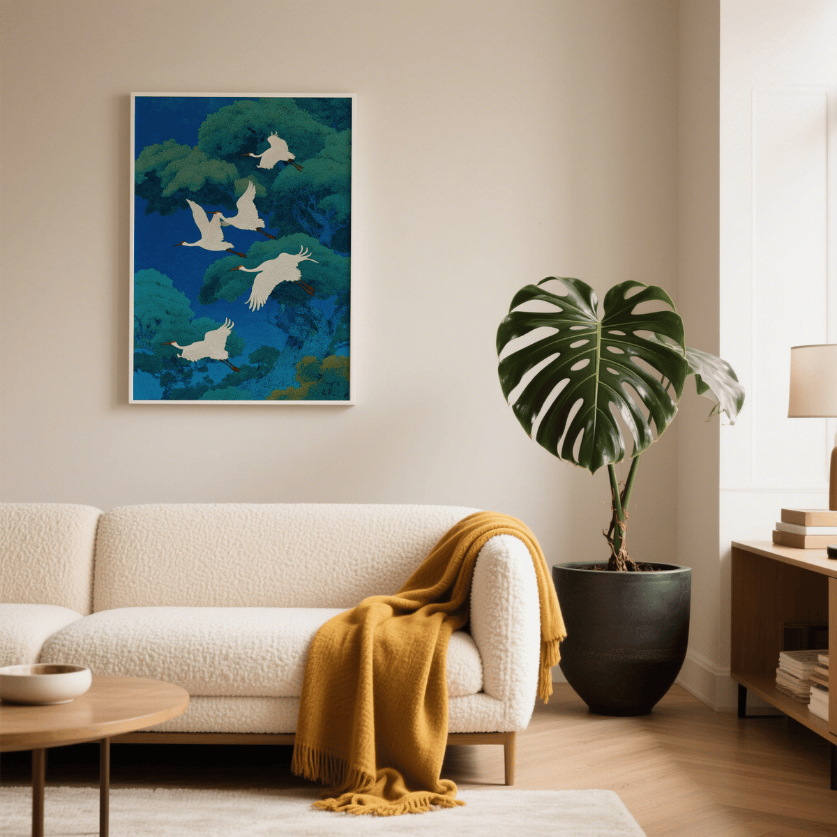 Bird art print of flying white cranes in blue and green Japanese-ink style above a cream sofa with a yellow throw