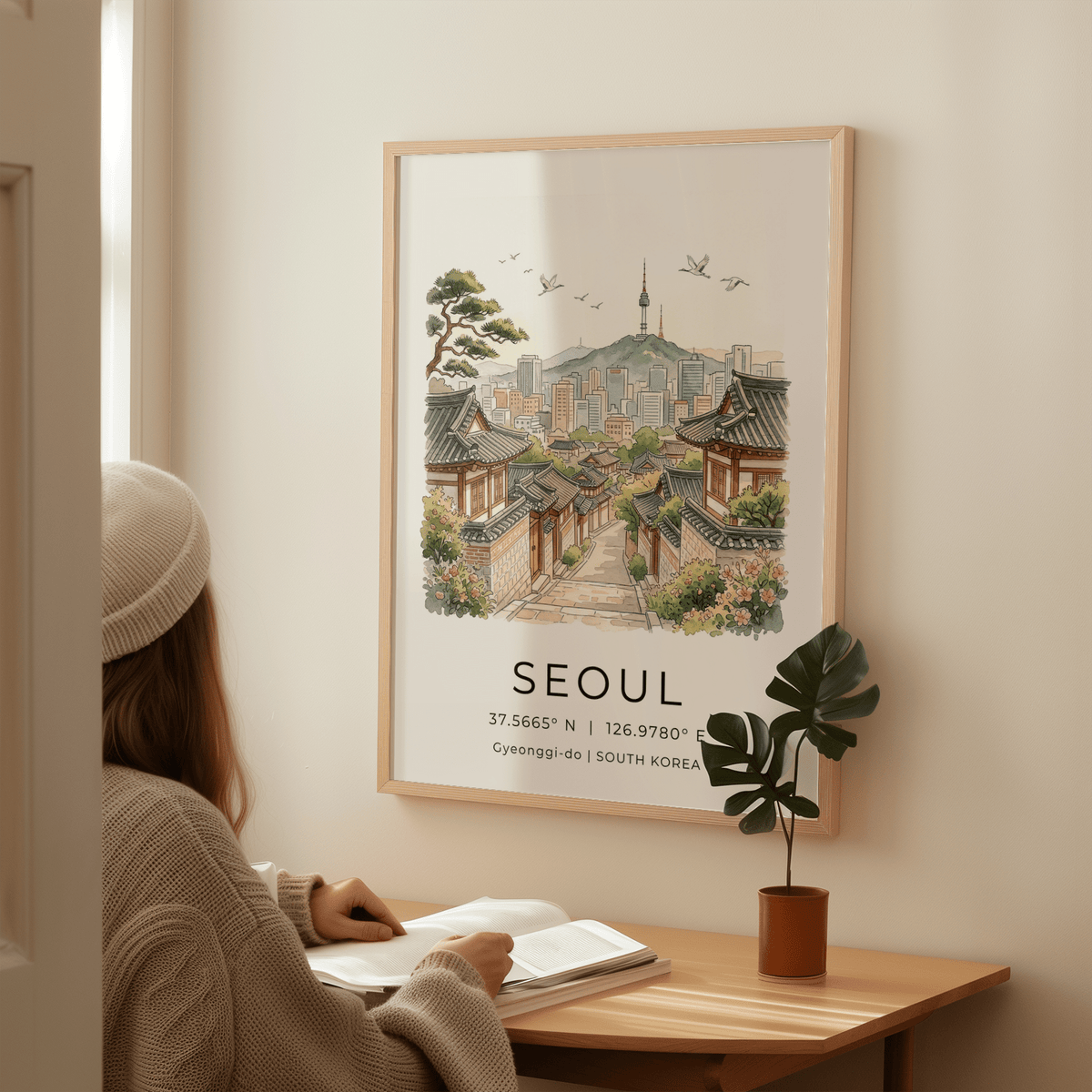 Framed Seoul Landscape Art Print illustrating traditional Korean houses and Seoul skyline with soft watercolour tones above a wooden desk