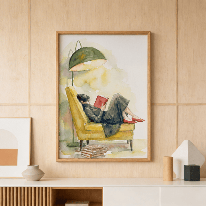 Framed Woman Reading In Armchair Print of a woman reading a red book on a yellow armchair with a green lamp above on a wooden wall