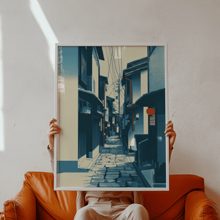 Framed Japanese Street wall art of a narrow Kyoto street in blue and cream held above an orange armchair