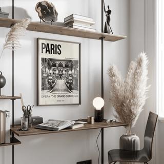 Print on a wall in a workspace of Paris Opera Art Print with monochrome staircase and typography near a desk lamp and pampas grass