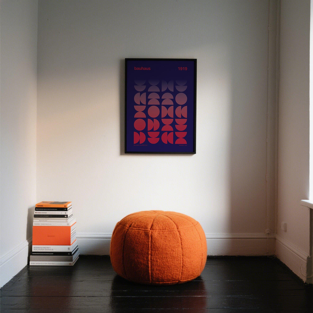 Graphic Design Poster on a wall with geometric gradient shapes in red and purple above an orange pouf and stacked books