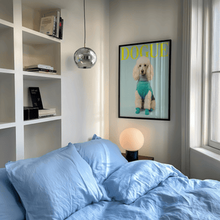 Pet wall decor of a white poodle in a turquoise sweater above a bedside lamp in a bedroom