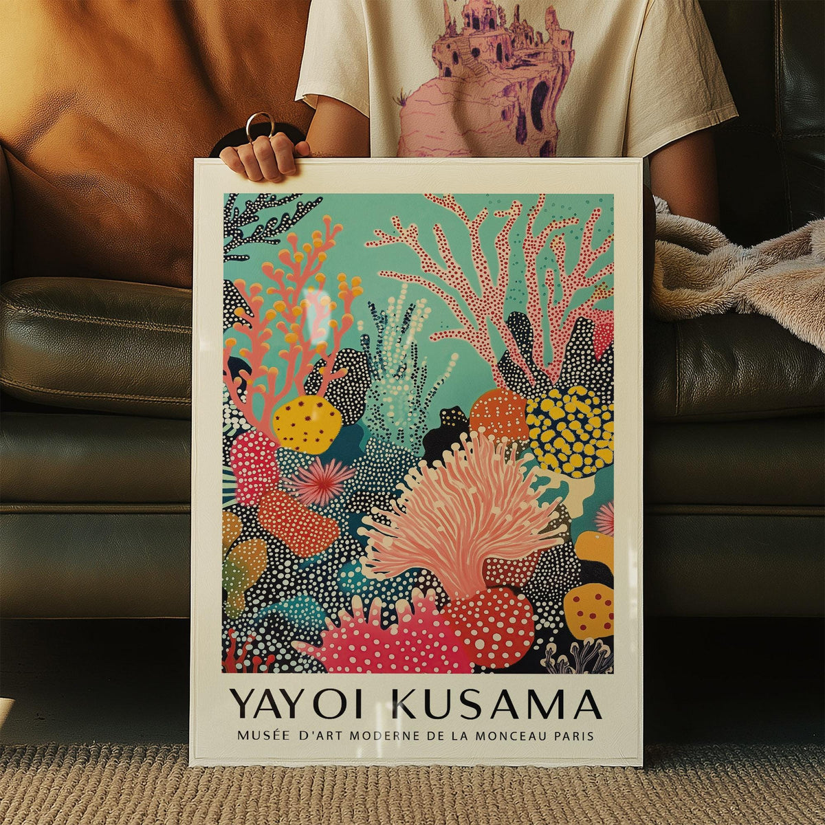 Bright wall art of abstract coral reef in turquoise, pink, yellow and black held in hands on sofa
