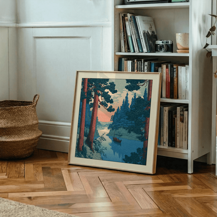 Print leaning on wooden floor of a river with a boat in blue and pink tones near bookshelf and basket