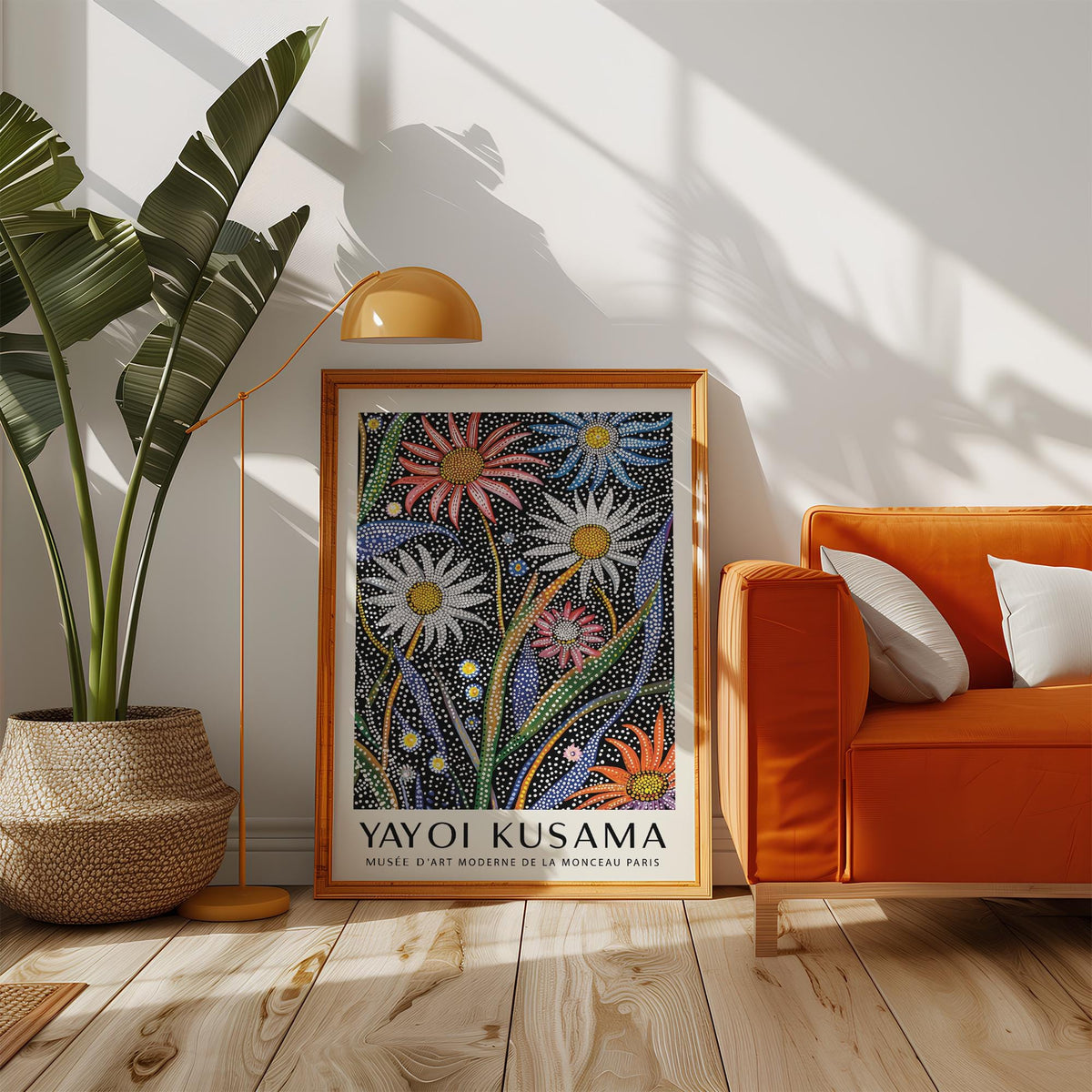 Abstract botanical wall art with dotted flowers in bright colours leaning on the floor next to an orange sofa