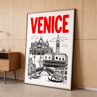 Framed Venice landmark art print with red text leaning on a wooden floor next to a small sideboard