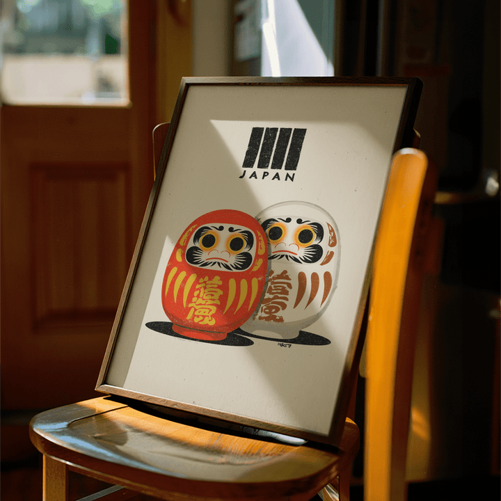Framed Daruma Print with red and white dolls in warm light on a wooden chair