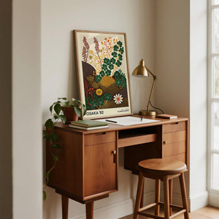 Print leaning on a wooden desk of clover and wildflowers in green and yellow beside a plant and lamp