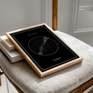Framed Custom Star Map print flat on a chair with light wood frame and black minimalist design
