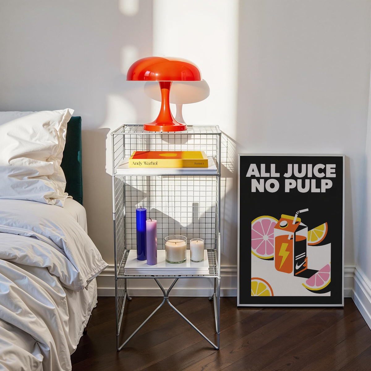 Pop Art Poster leaning on floor next to a bedside table with a red lamp and candles in a bedroom