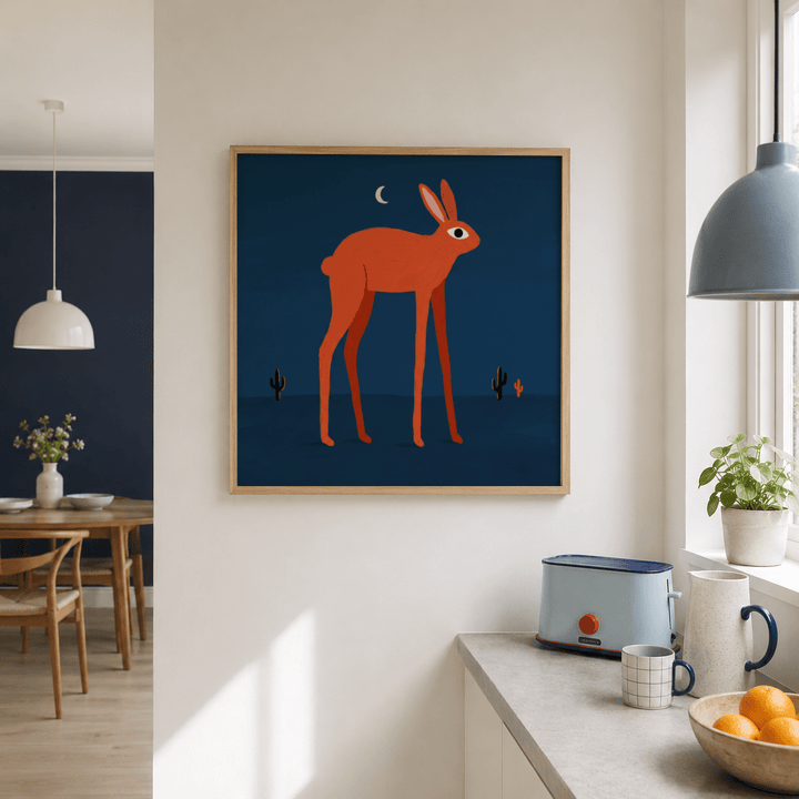 Print on a wall of an orange rabbit with a moon above in blue tones in a kitchen near a toaster and window