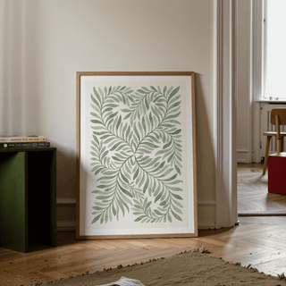 Print of green leaf art in minimalist watercolour leaning against wall near books on green side table in living room