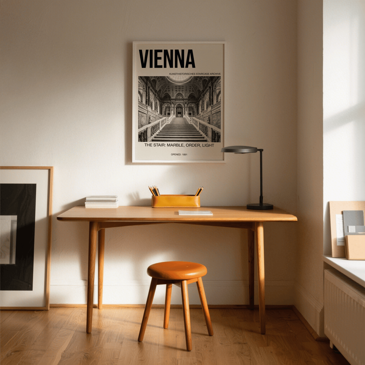 Vienna Architecture Art Print above a wooden desk with brown stool and black desk lamp in a warm lit room