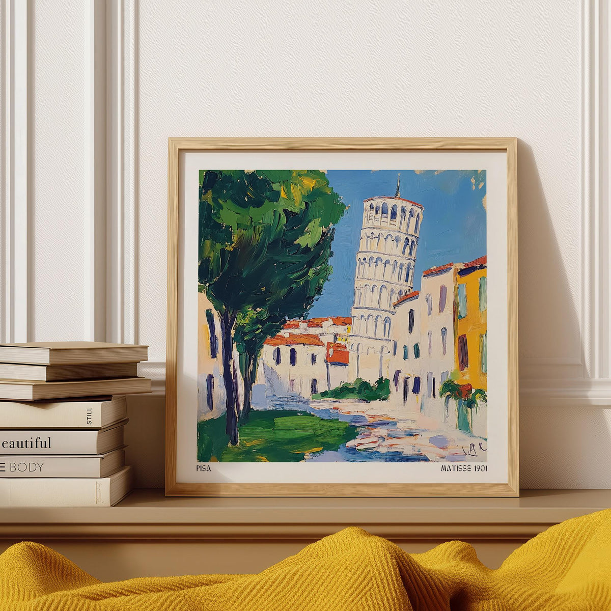 Framed Leaning Tower of Pisa Pictures with green trees and blue sky leaning on a mantelpiece next to books