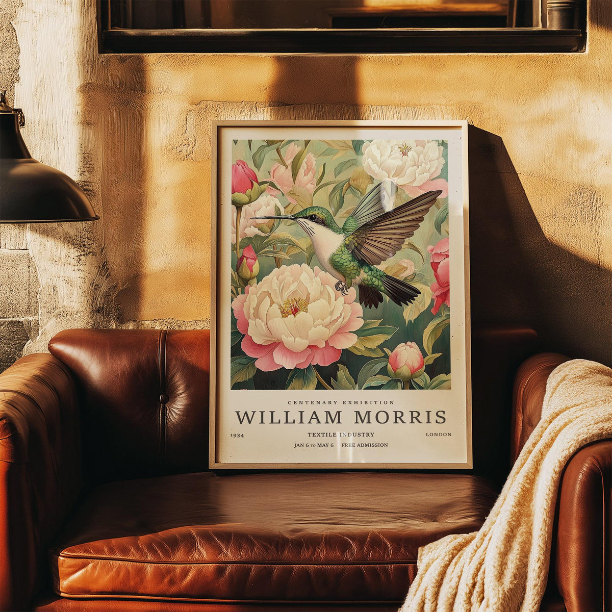 Hummingbird prints showing a framed illustration of a hummingbird and pink peonies resting on a leather sofa with a throw
