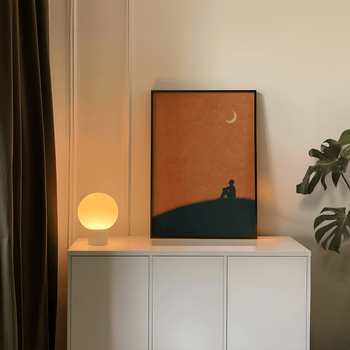 Night Silhouette Poster print leaning on a white cabinet with a glowing lamp and green plant