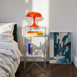 Japanese Street wall art leaning on floor next to bedside table with orange lamp and candles