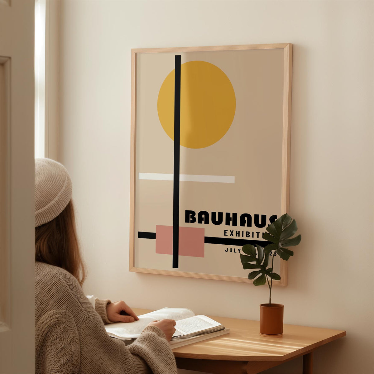 Office Prints with abstract geometric shapes in yellow and pink above a wooden desk with a small plant