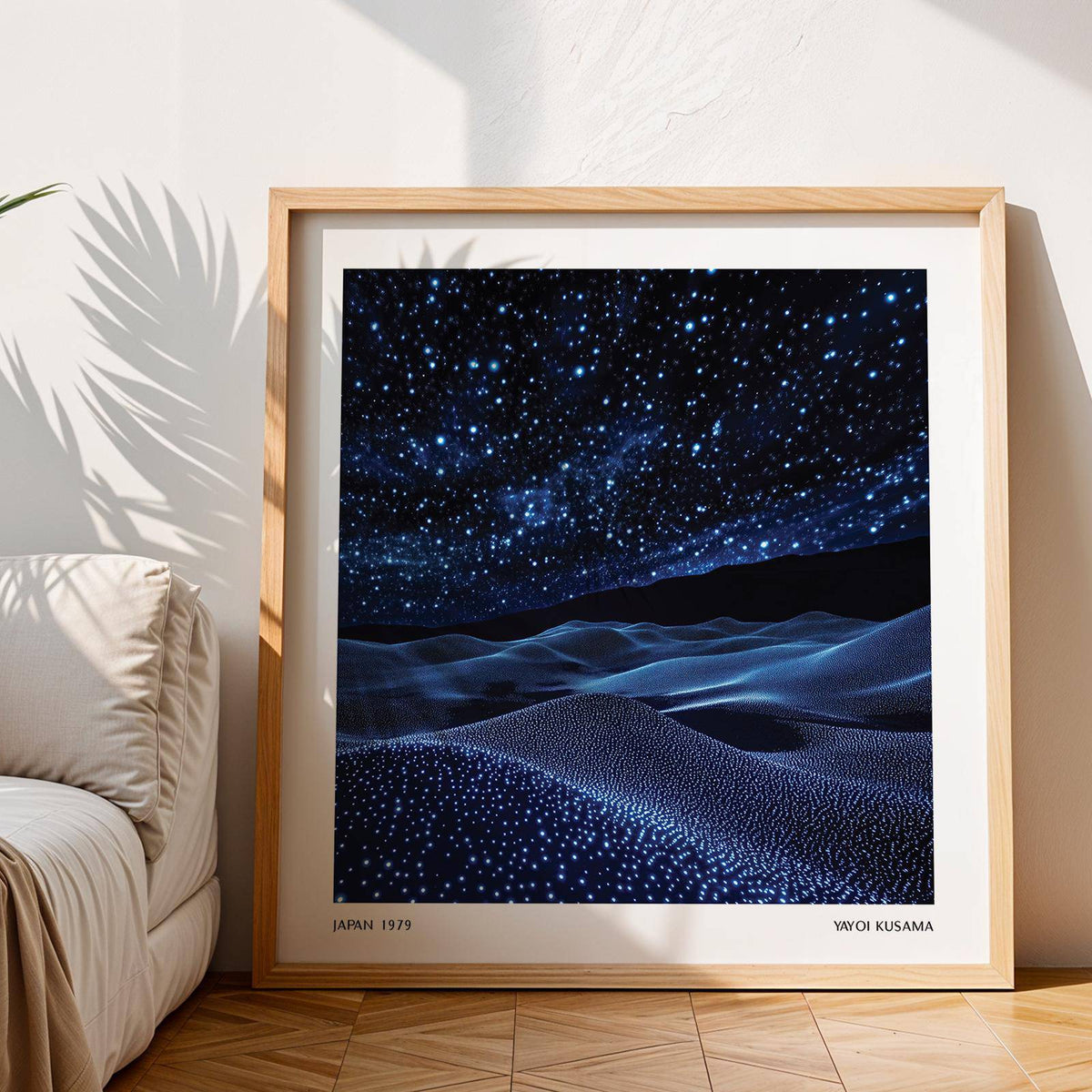 Framed navy blue artwork of starry night sky and dunes leaning on the floor by a sofa