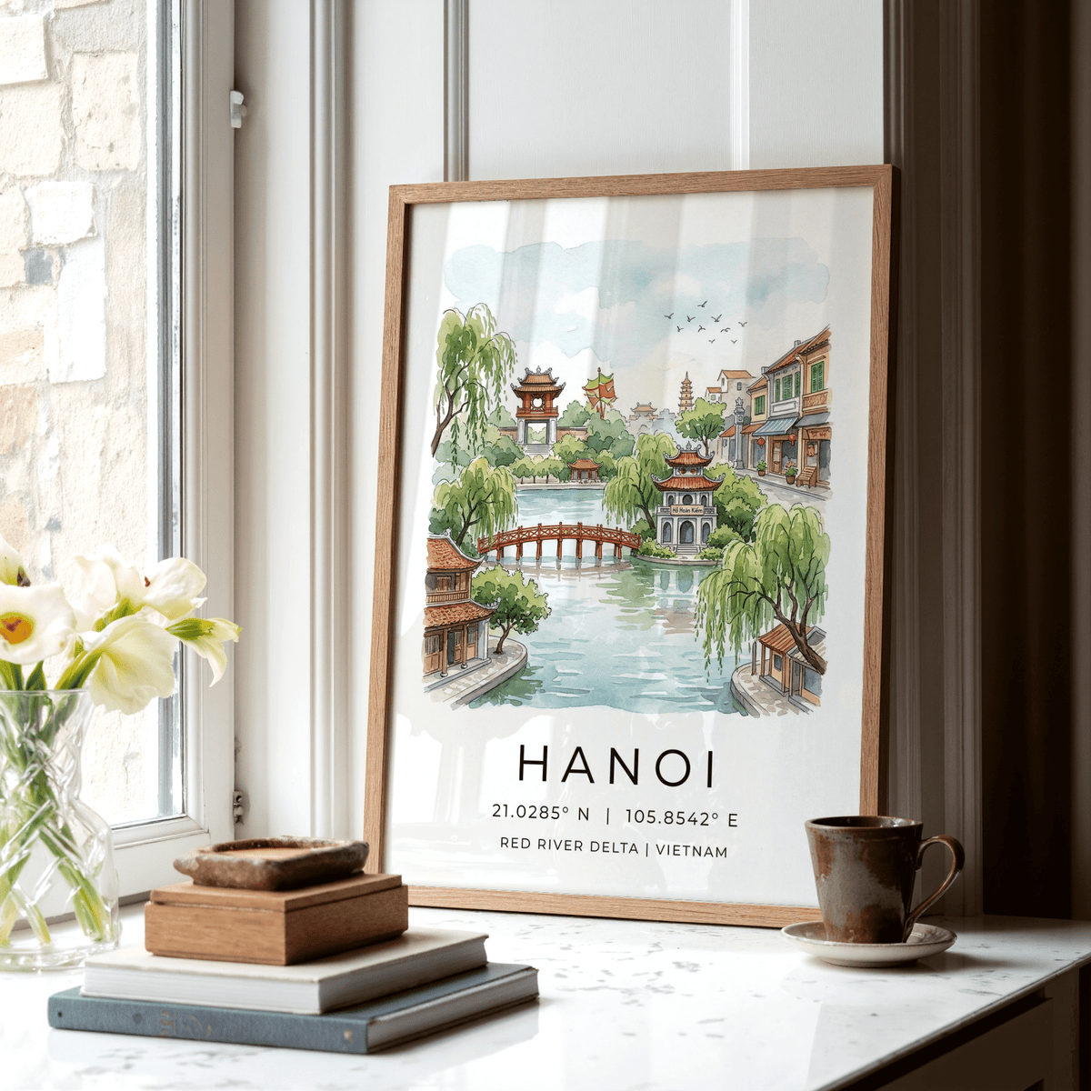 Hanoi landscape wall art in watercolour leaning on a windowsill with a cup and books nearby