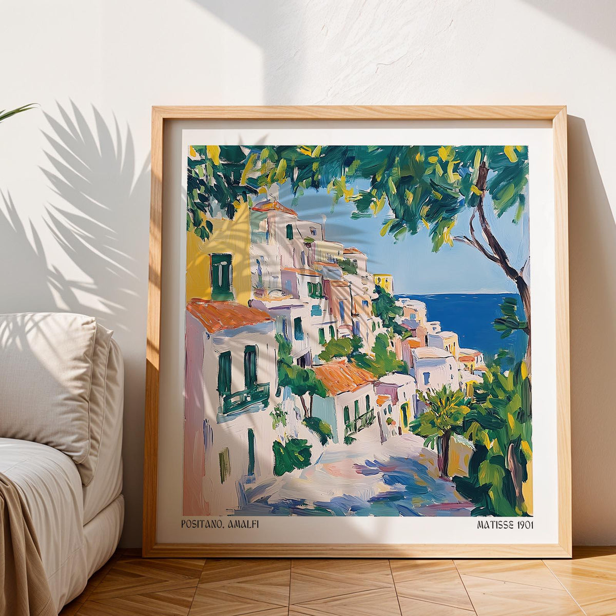 Framed Positano Art of an Italian coastal village with blue sea and green trees near a sofa