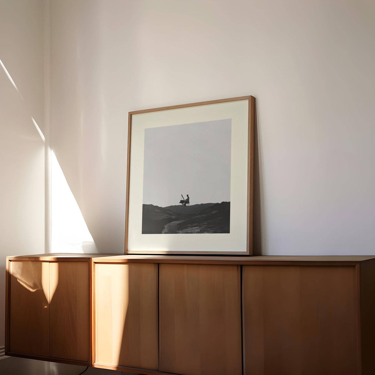 Framed print of piano abstract art with a black silhouette playing piano on a grey background resting on a wood cupboard