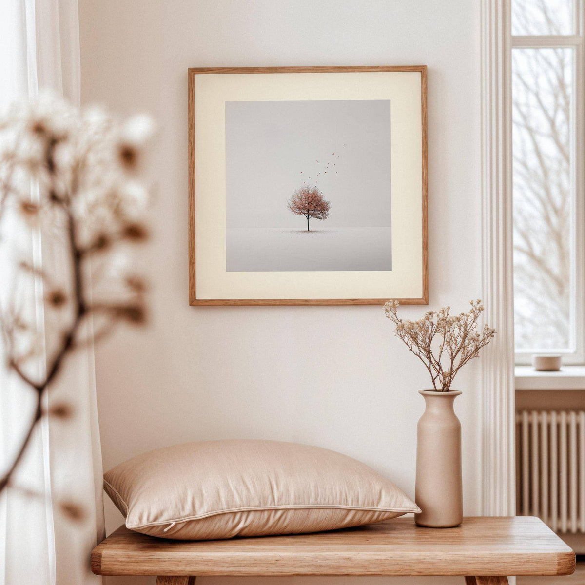 Tree wall art of a solitary bare tree with falling leaves above a wooden table with a beige cushion and vase