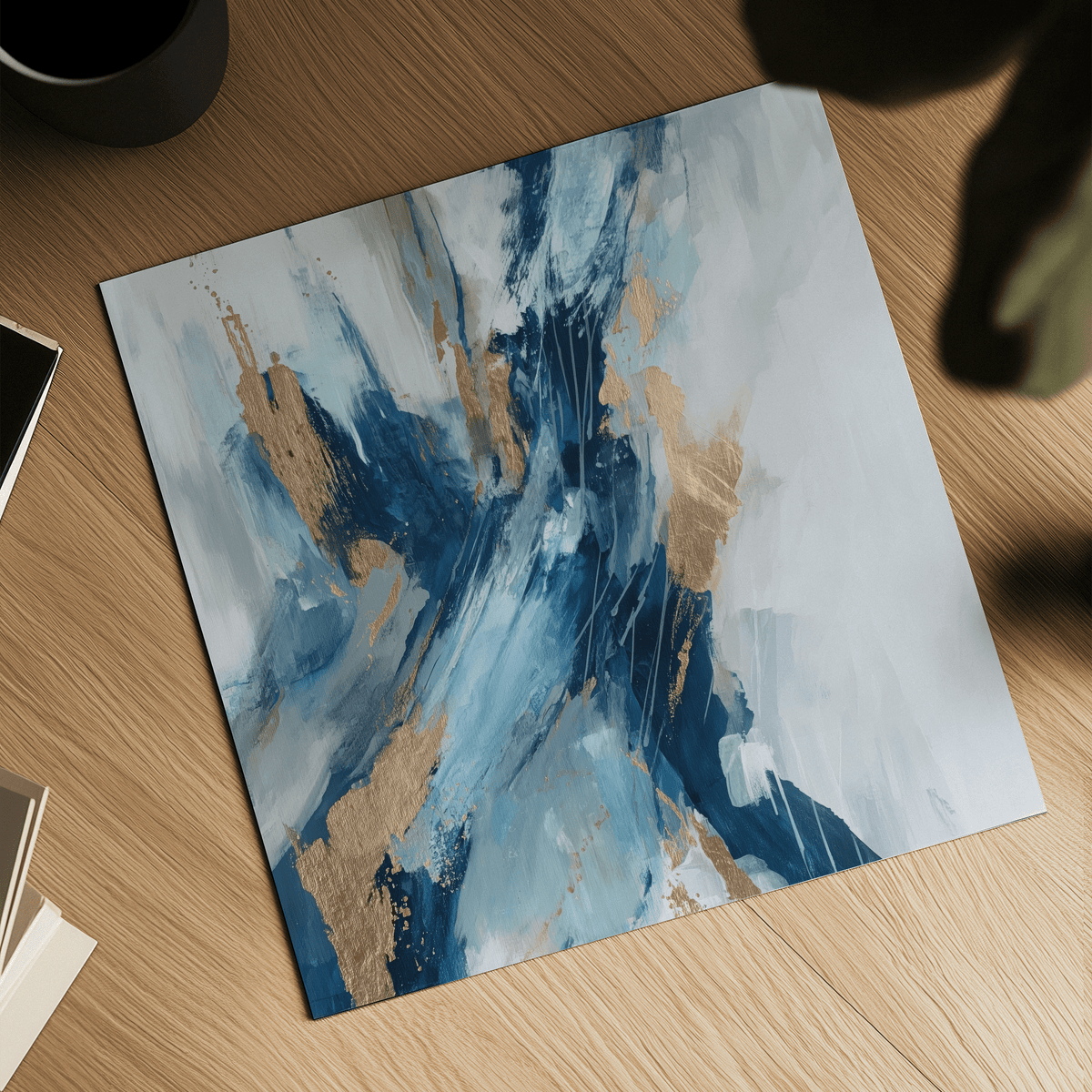 Blue abstract wall art with gold and blue splashes laid on wooden surface near books