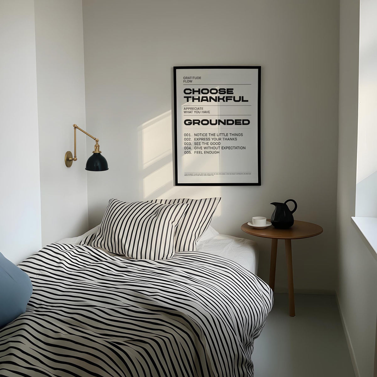 Print on a wall in a bedroom with thankful gratitude text beside a wooden side table with black teapot