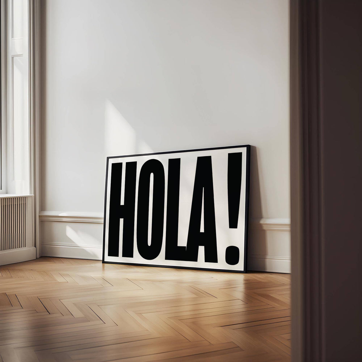 Typographic posters featuring HOLA typography in black and white leaning on wooden floor near a window