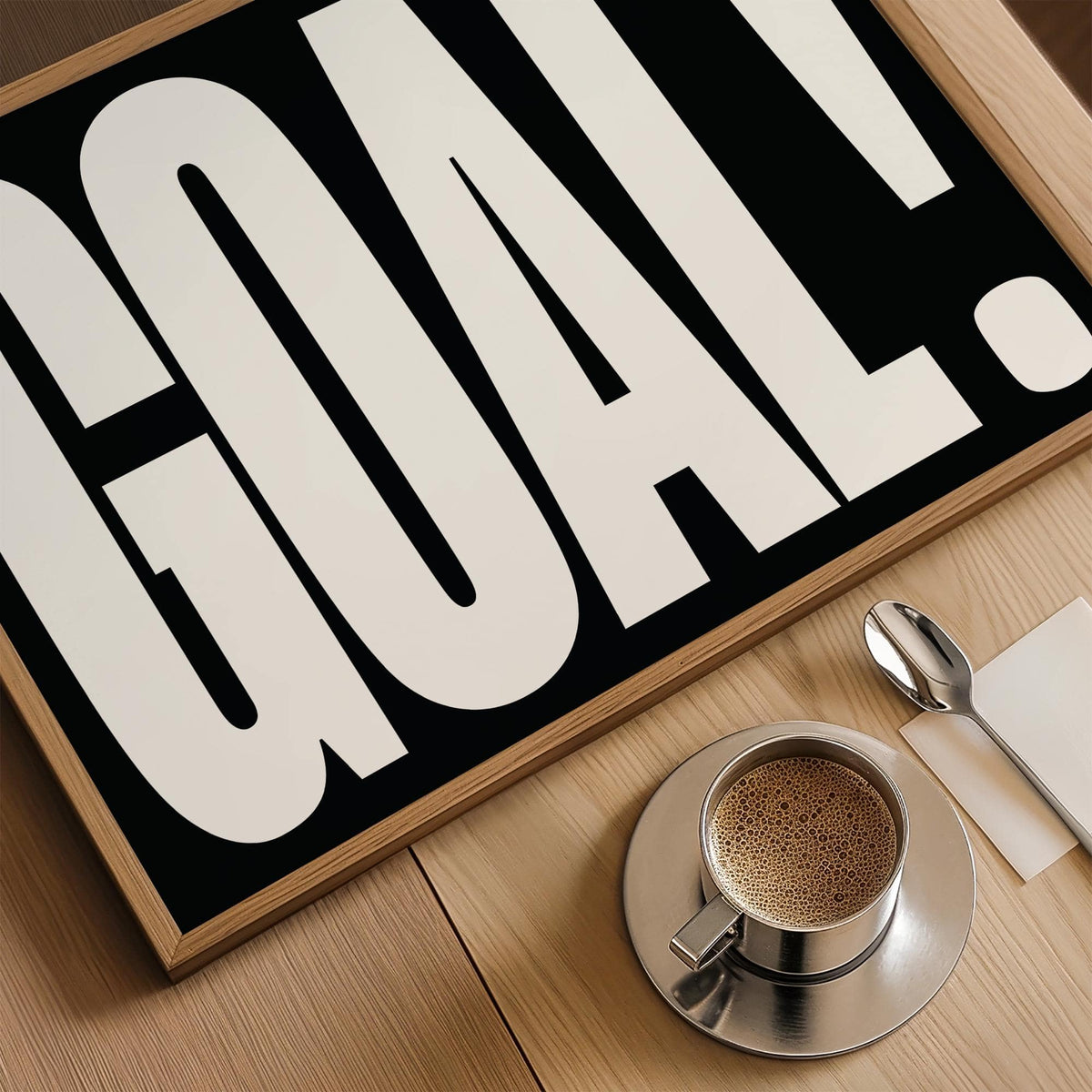 Framed Goal Poster close-up with black and white typography on a wooden table with coffee cup