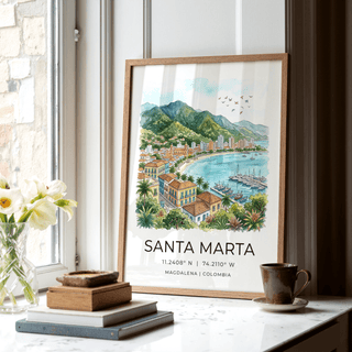 Print leaning on a white marble windowsill showing a watercolour Santa Marta coastline with green mountains and turquoise sea
